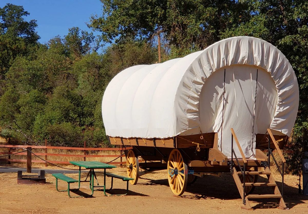 Glamping covered wagon with canvas cover, spoked wheels and entry steps at a campsite
